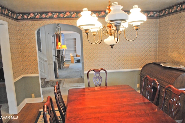 dining space featuring wallpapered walls, arched walkways, an inviting chandelier, and wainscoting