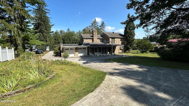 view of front of house featuring driveway, a chimney, an attached garage, fence, and a front lawn