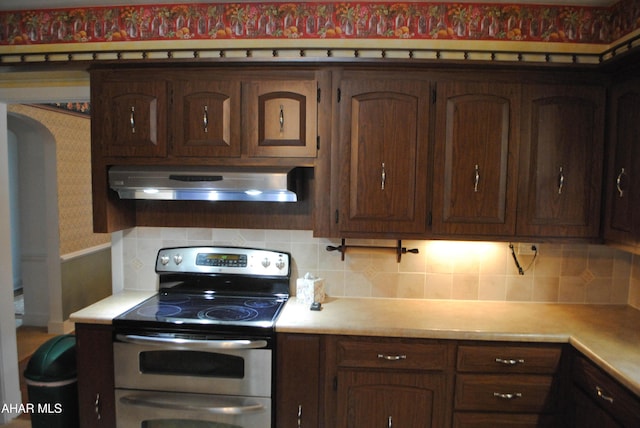 kitchen with tasteful backsplash, exhaust hood, light countertops, double oven range, and wallpapered walls