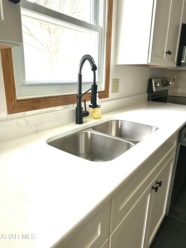 interior details featuring a sink, light countertops, tasteful backsplash, and white cabinets