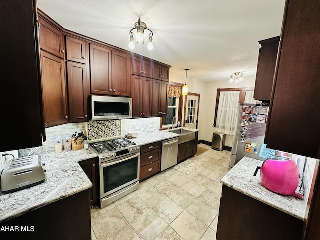 kitchen with decorative light fixtures, sink, decorative backsplash, light stone counters, and stainless steel appliances