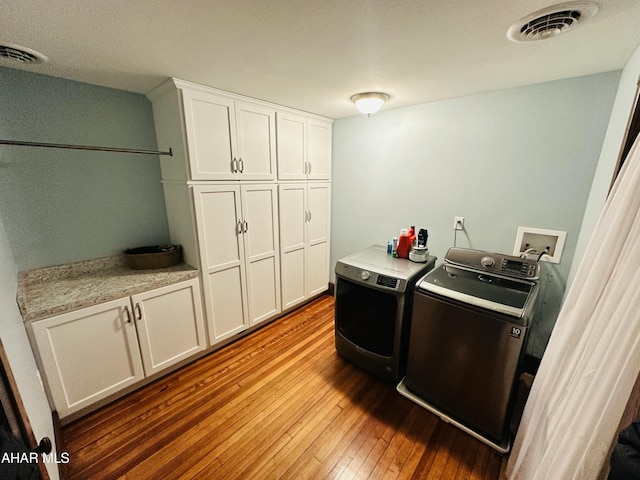 clothes washing area with cabinets, washing machine and dryer, and light wood-type flooring