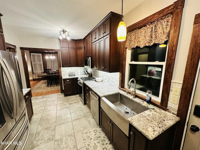 kitchen with sink, hanging light fixtures, appliances with stainless steel finishes, light stone countertops, and decorative backsplash