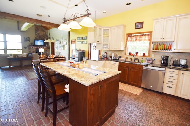 kitchen featuring stainless steel dishwasher, dark stone counters, decorative light fixtures, a center island, and a breakfast bar area