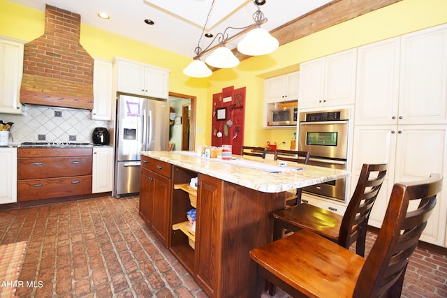 kitchen featuring light stone countertops, stainless steel appliances, an island with sink, pendant lighting, and custom range hood