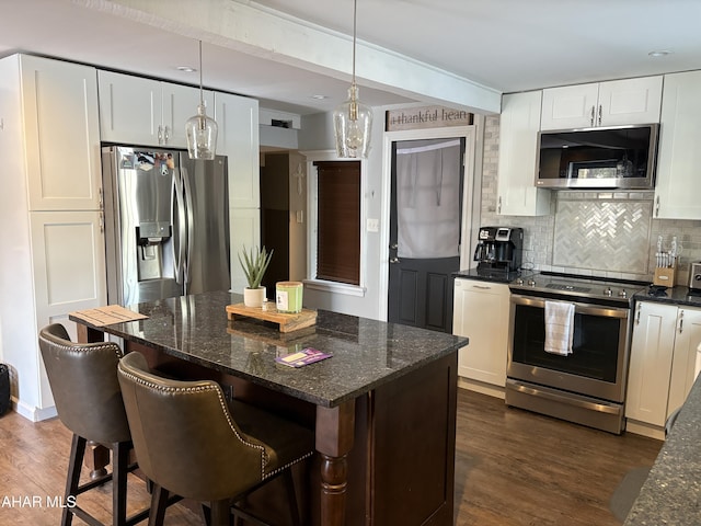 kitchen featuring pendant lighting, white cabinetry, stainless steel appliances, and dark stone countertops