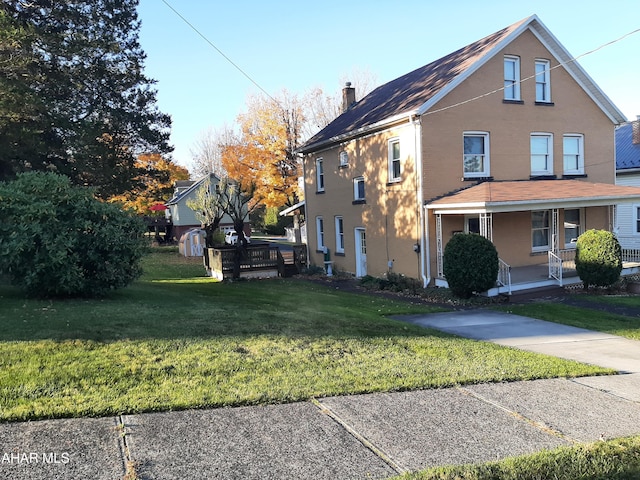 view of side of property featuring covered porch, a yard, and a chimney