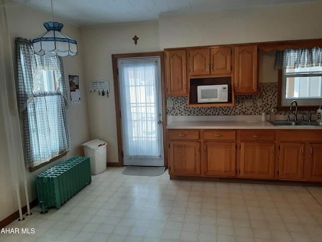 kitchen featuring white microwave, radiator heating unit, decorative light fixtures, light countertops, and a sink