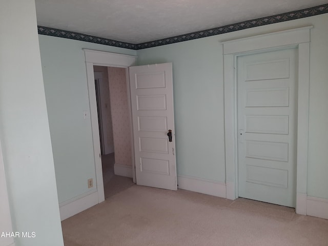 spare room with light colored carpet, a textured ceiling, and baseboards