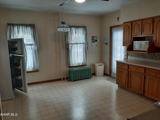 unfurnished dining area with light floors, a ceiling fan, a wealth of natural light, and radiator