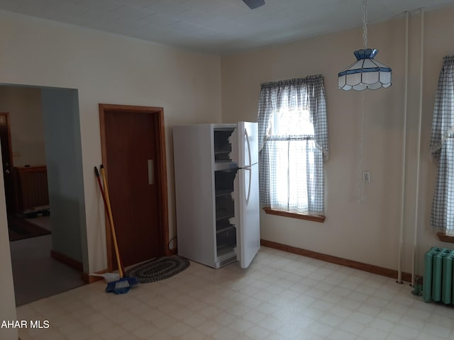 unfurnished bedroom featuring light floors, radiator heating unit, baseboards, and freestanding refrigerator