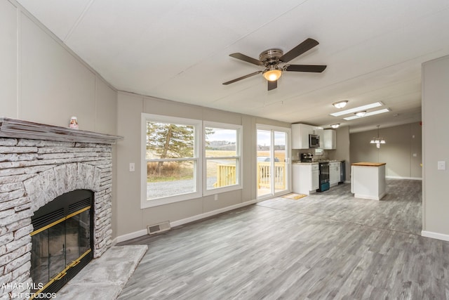 unfurnished living room featuring light hardwood / wood-style flooring, a stone fireplace, and ceiling fan