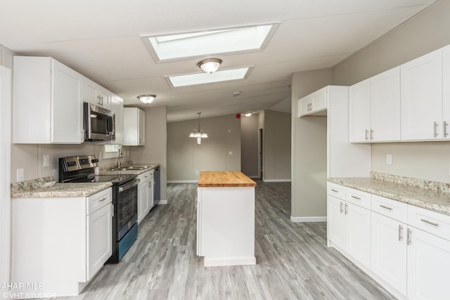 kitchen featuring wooden counters, white cabinets, light hardwood / wood-style flooring, vaulted ceiling with skylight, and stainless steel appliances