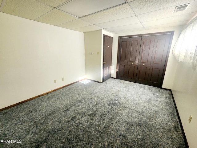 unfurnished bedroom featuring visible vents, baseboards, a drop ceiling, a closet, and carpet flooring