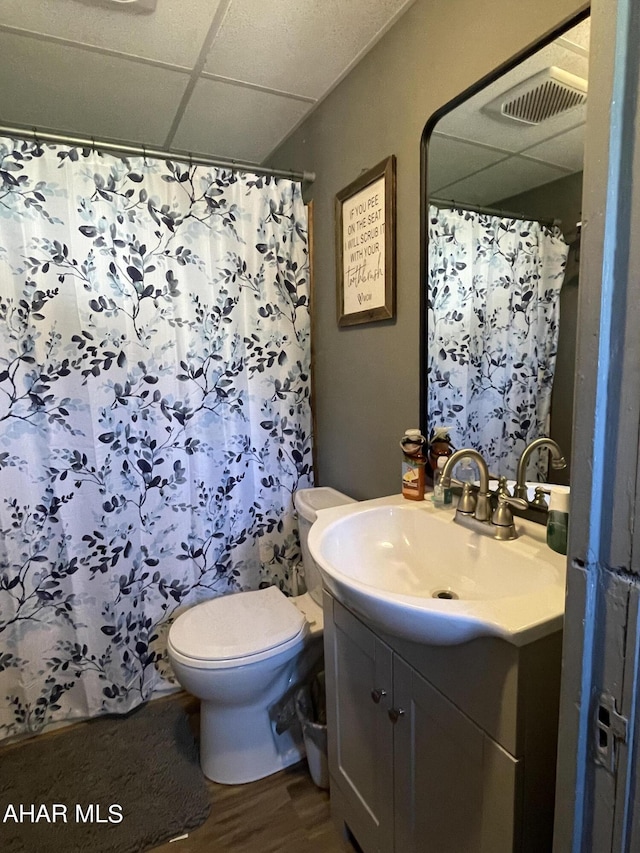 bathroom with hardwood / wood-style floors, a drop ceiling, toilet, and vanity