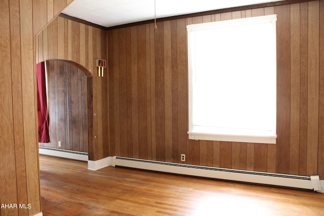 unfurnished room featuring wood walls, light wood-type flooring, and a baseboard heating unit