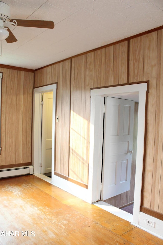 empty room featuring baseboard heating, ceiling fan, and wooden walls