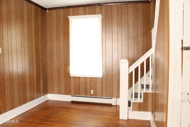 empty room with baseboard heating, wooden walls, and hardwood / wood-style flooring