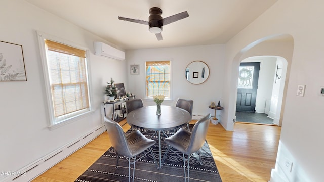 dining area with light wood-type flooring, a wall unit AC, a wealth of natural light, and a baseboard heating unit