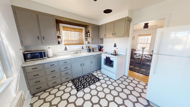 kitchen with gray cabinetry, white appliances, backsplash, sink, and light hardwood / wood-style flooring