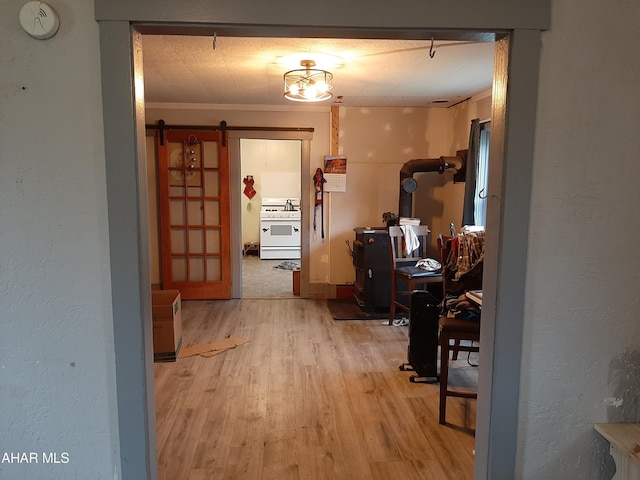 corridor featuring a textured ceiling, a barn door, light hardwood / wood-style floors, and ornamental molding