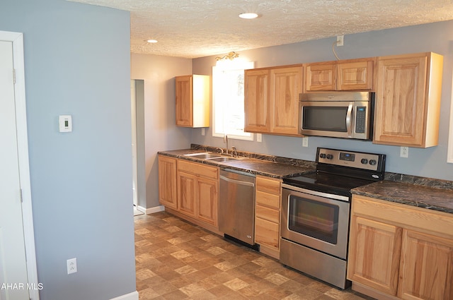 kitchen with appliances with stainless steel finishes, a textured ceiling, light brown cabinets, and sink