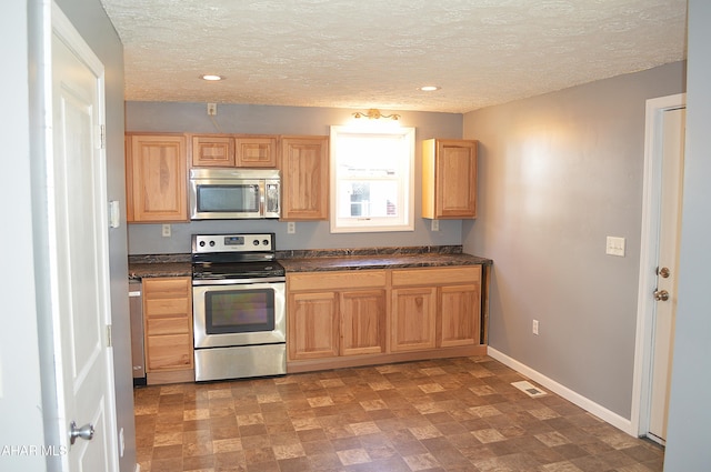 kitchen with a textured ceiling, stainless steel appliances, and light brown cabinetry