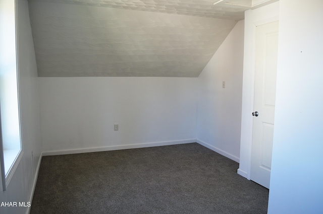 additional living space with vaulted ceiling and dark colored carpet