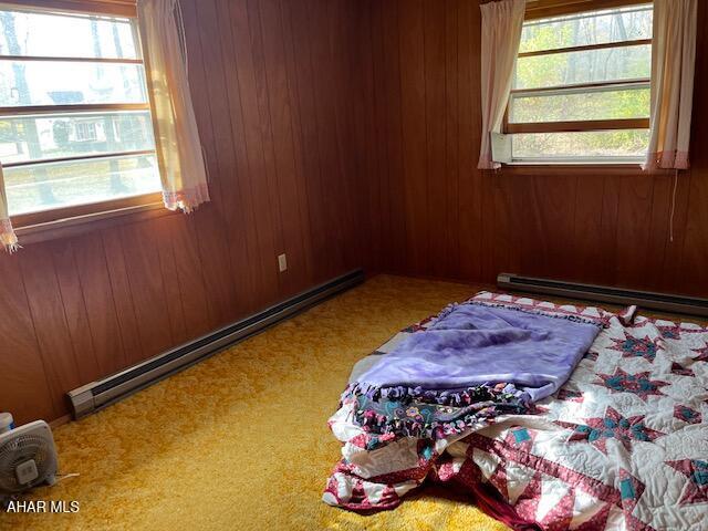 bedroom featuring wooden walls, a baseboard radiator, and multiple windows