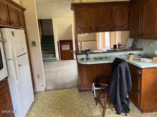 kitchen with kitchen peninsula, white fridge, and light colored carpet