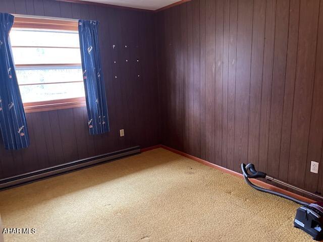 spare room with carpet floors, baseboard heating, and wooden walls