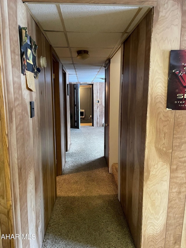 hall with carpet flooring, wooden walls, and a drop ceiling