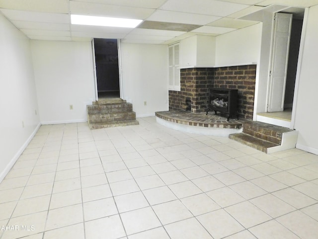 unfurnished living room featuring a wood stove, light tile patterned floors, and a drop ceiling