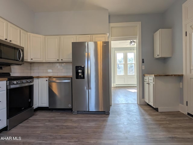 kitchen with appliances with stainless steel finishes, a baseboard heating unit, white cabinetry, and backsplash