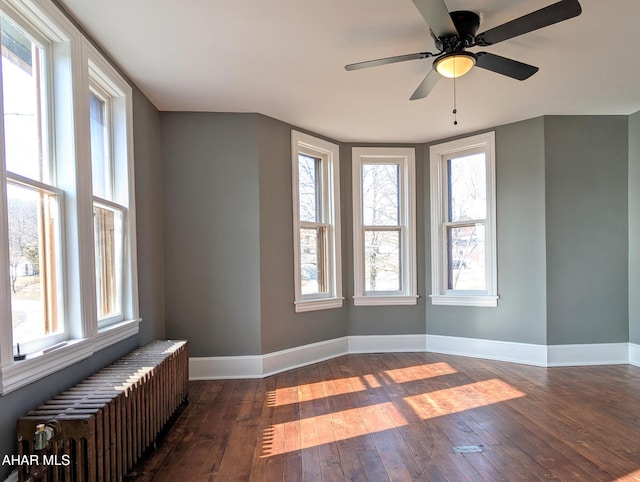 empty room with radiator, dark wood-type flooring, and a wealth of natural light