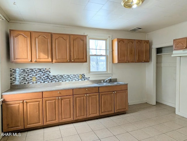 kitchen featuring sink, backsplash, light tile patterned floors, and crown molding