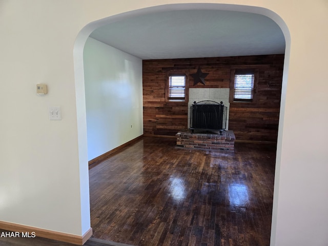 unfurnished living room with dark hardwood / wood-style flooring, a brick fireplace, and wood walls