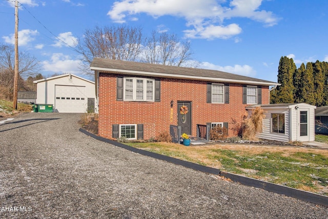 raised ranch featuring gravel driveway, brick siding, an outdoor structure, and a detached garage