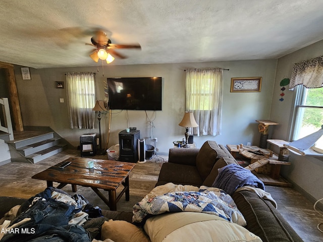 living room featuring a wood stove, ceiling fan, hardwood / wood-style floors, and a textured ceiling