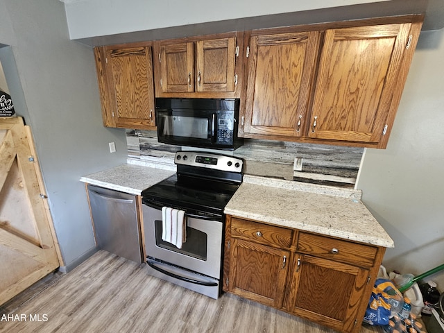 kitchen featuring stainless steel appliances, light hardwood / wood-style flooring, and light stone counters