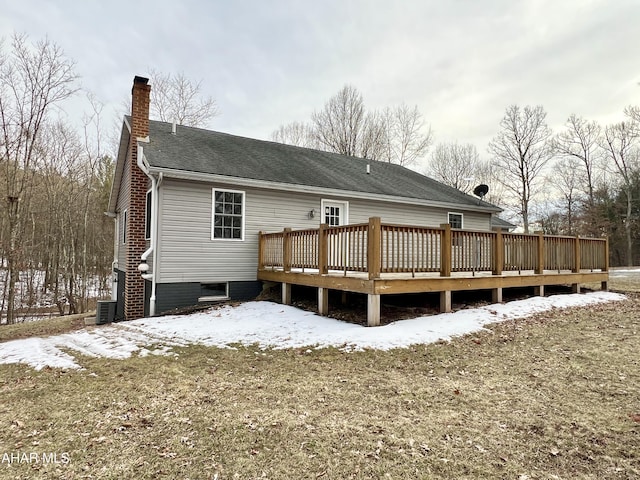 snow covered rear of property with a shingled roof, a chimney, central AC unit, and a wooden deck