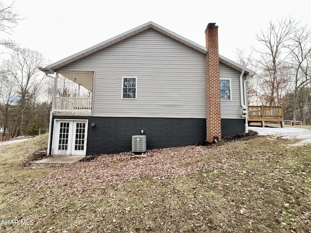 view of side of property featuring french doors, a chimney, a balcony, and central AC unit