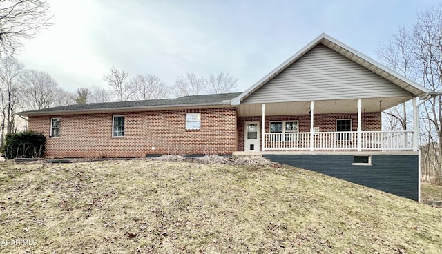 back of property with covered porch, brick siding, and a lawn