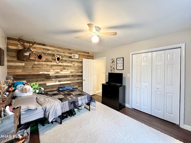 bedroom with baseboards, ceiling fan, wood finished floors, wood walls, and a closet