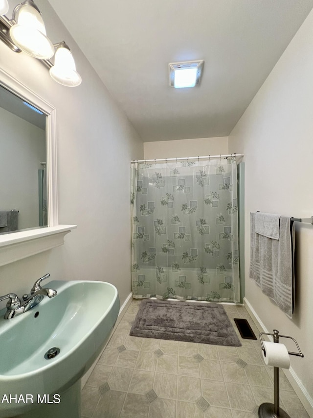 bathroom featuring curtained shower, baseboards, visible vents, and a sink