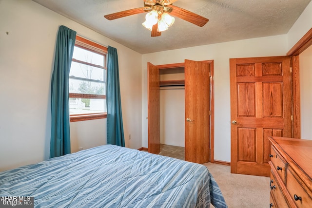 bedroom with ceiling fan, a closet, a textured ceiling, and light colored carpet