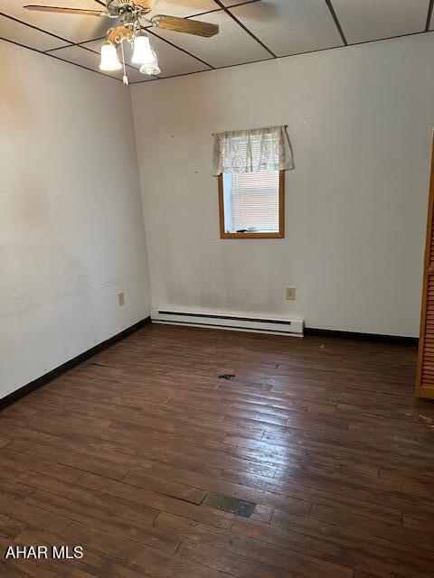 empty room featuring baseboard heating, ceiling fan, a drop ceiling, and dark hardwood / wood-style floors