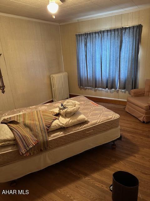 bedroom featuring hardwood / wood-style flooring, radiator, and crown molding