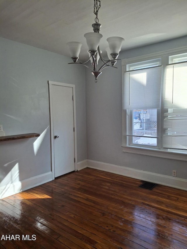 empty room featuring plenty of natural light, a chandelier, and dark hardwood / wood-style flooring