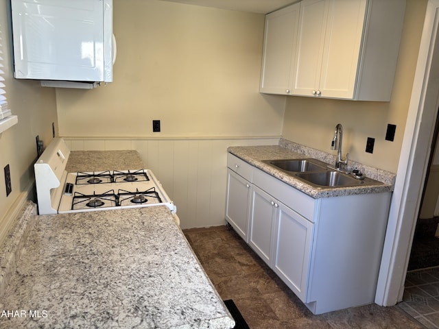 kitchen with white range with gas cooktop, sink, and white cabinets